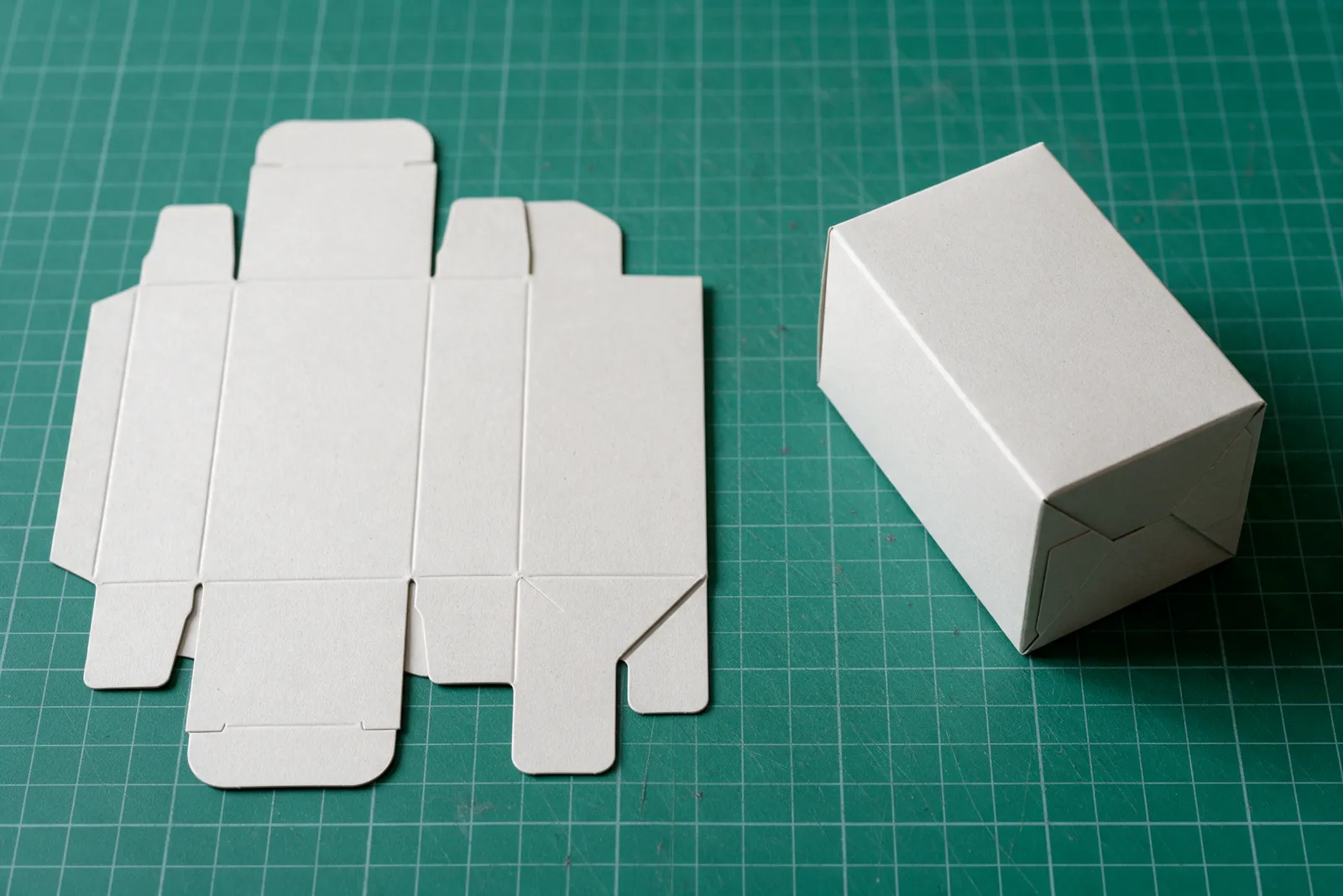 Flat die-cut box blank on a cutting mat next to the folded box