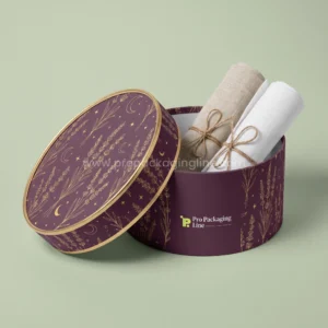 Custom bed sheet box: plum rigid round hatbox-style box holding rolled linen sheets, gold lavender and moon artwork, Pro Packaging Line logo