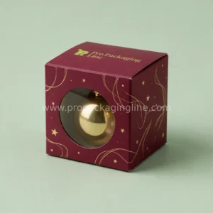Burgundy ornament box with round window showing gold bauble